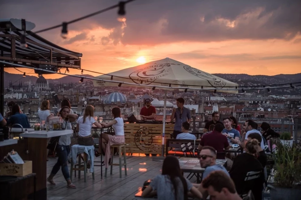 Trendy crowds enjoying cocktails at the 360 Bar rooftop with a stunning background of the Budapest skyline