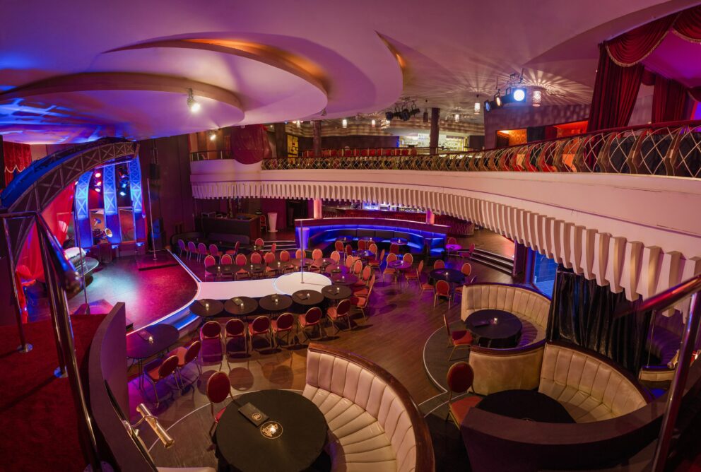 A sophisticated two-story club featuring a main dancing pole stage and curved semicircular booths