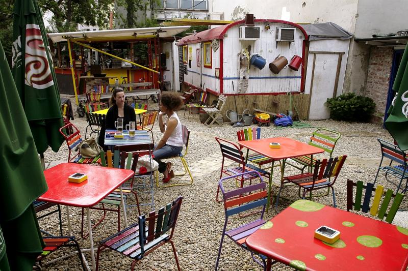 Red tables and colorful chairs with the built-in circus wagon at Kőleves Kert garden bar in Budapest