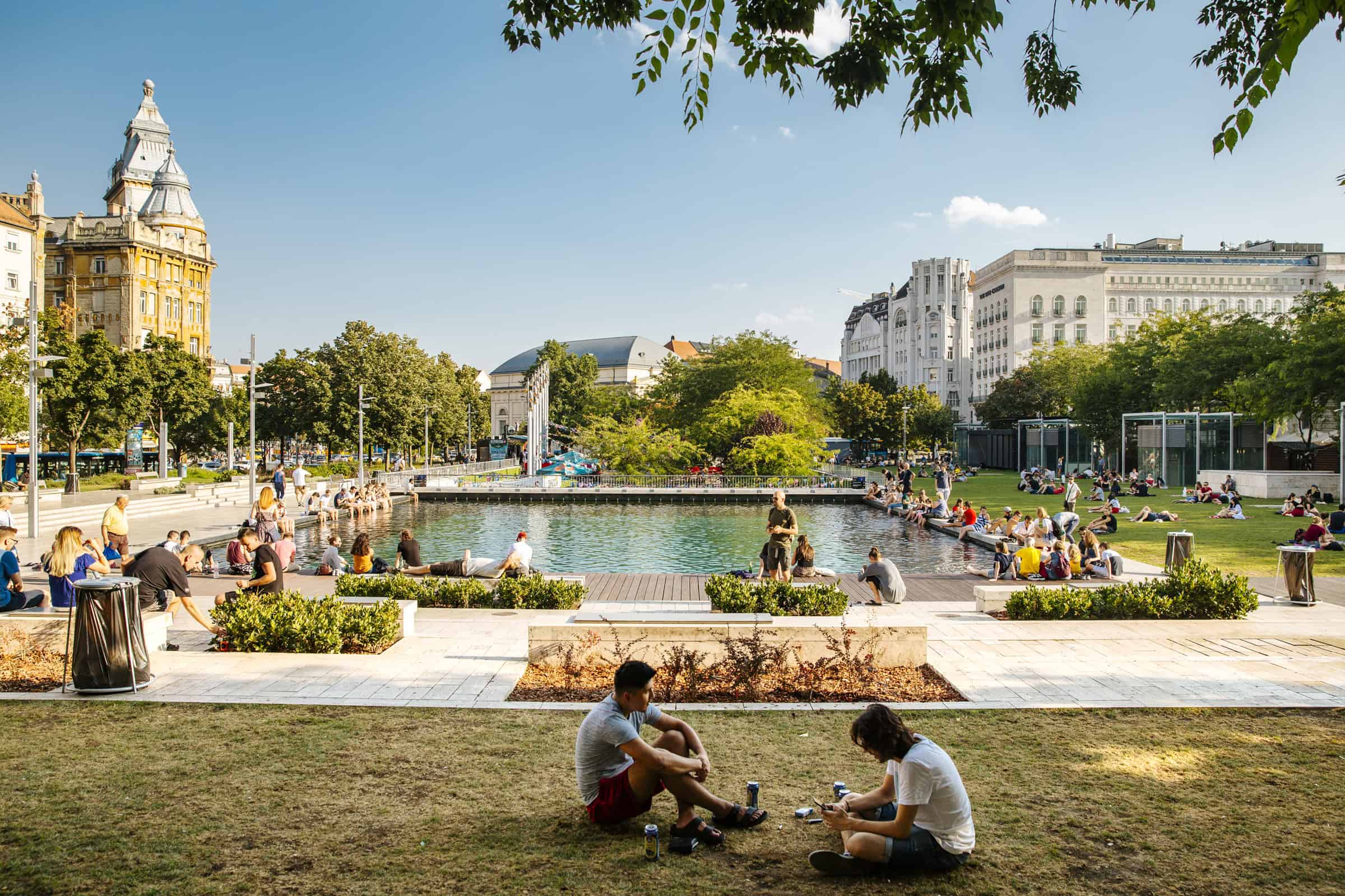 People sitting and relaxing by the glass-bottomed pool of Akvarium Klub in Budapest's Erzsebet Square on a sunny day.
