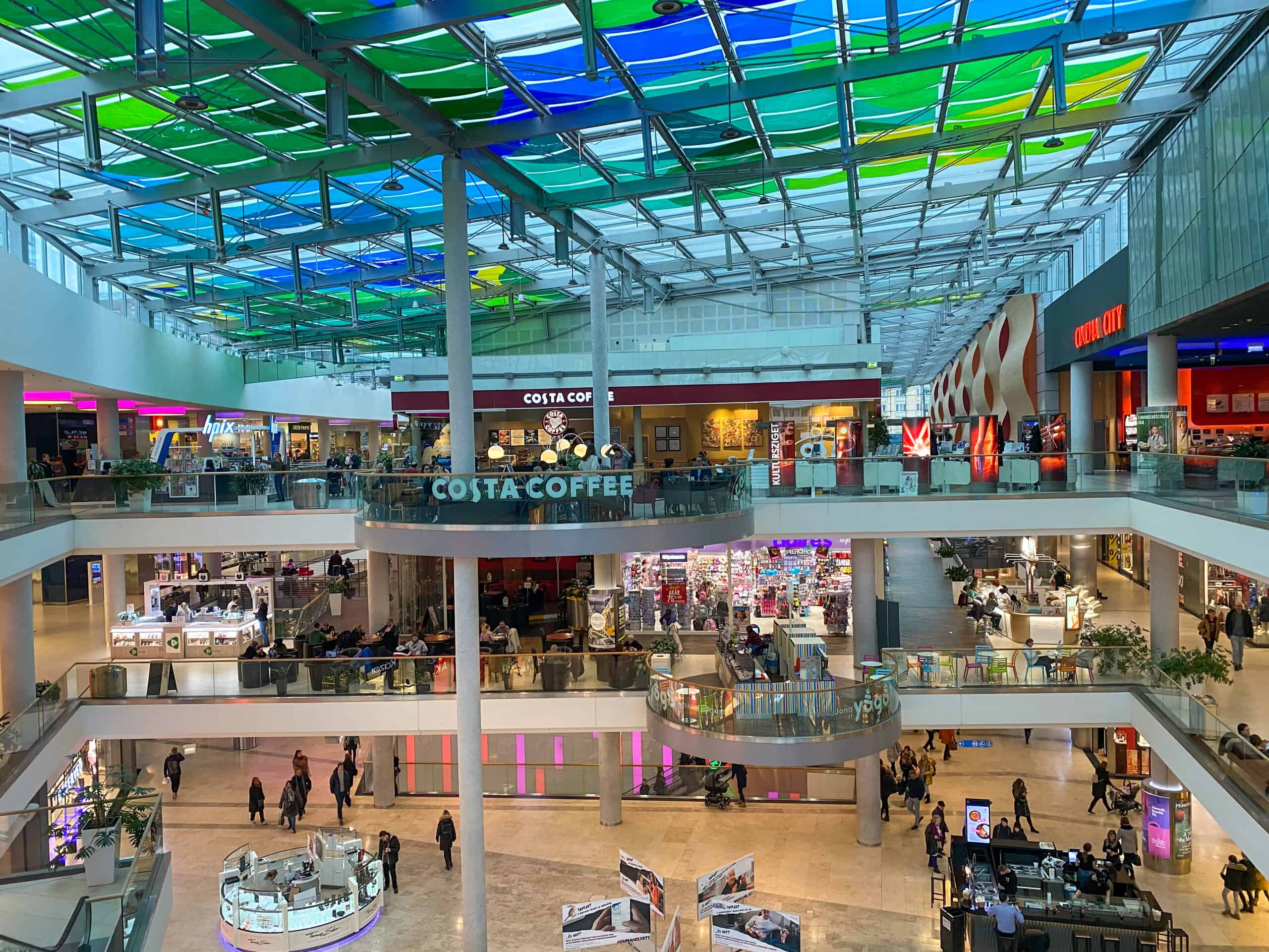 The bright interior atrium of Allee Mall with its colorful ceiling and Costa Coffee kiosk