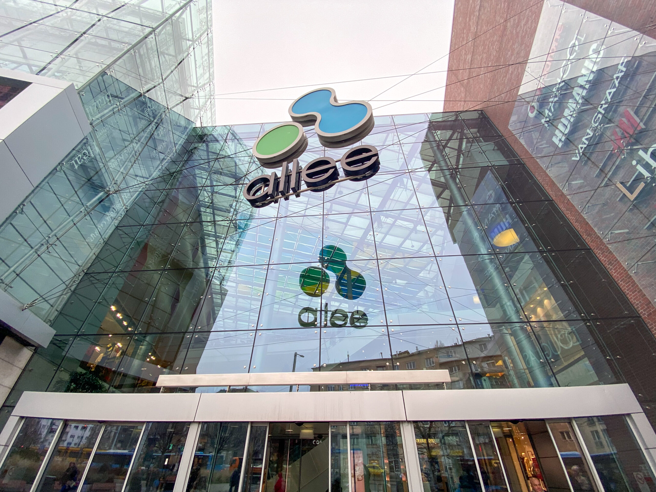 Close-up of the Allee Mall logo on its glass facade