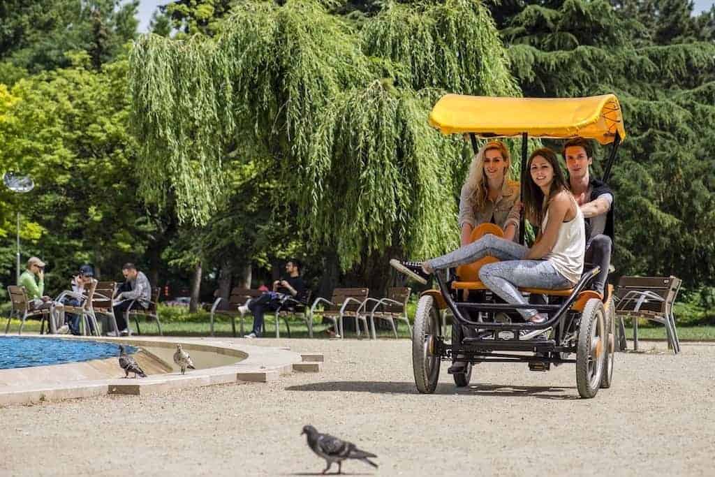 Friends riding a yellow pedal quadricycle through the green parks of Margaret Island