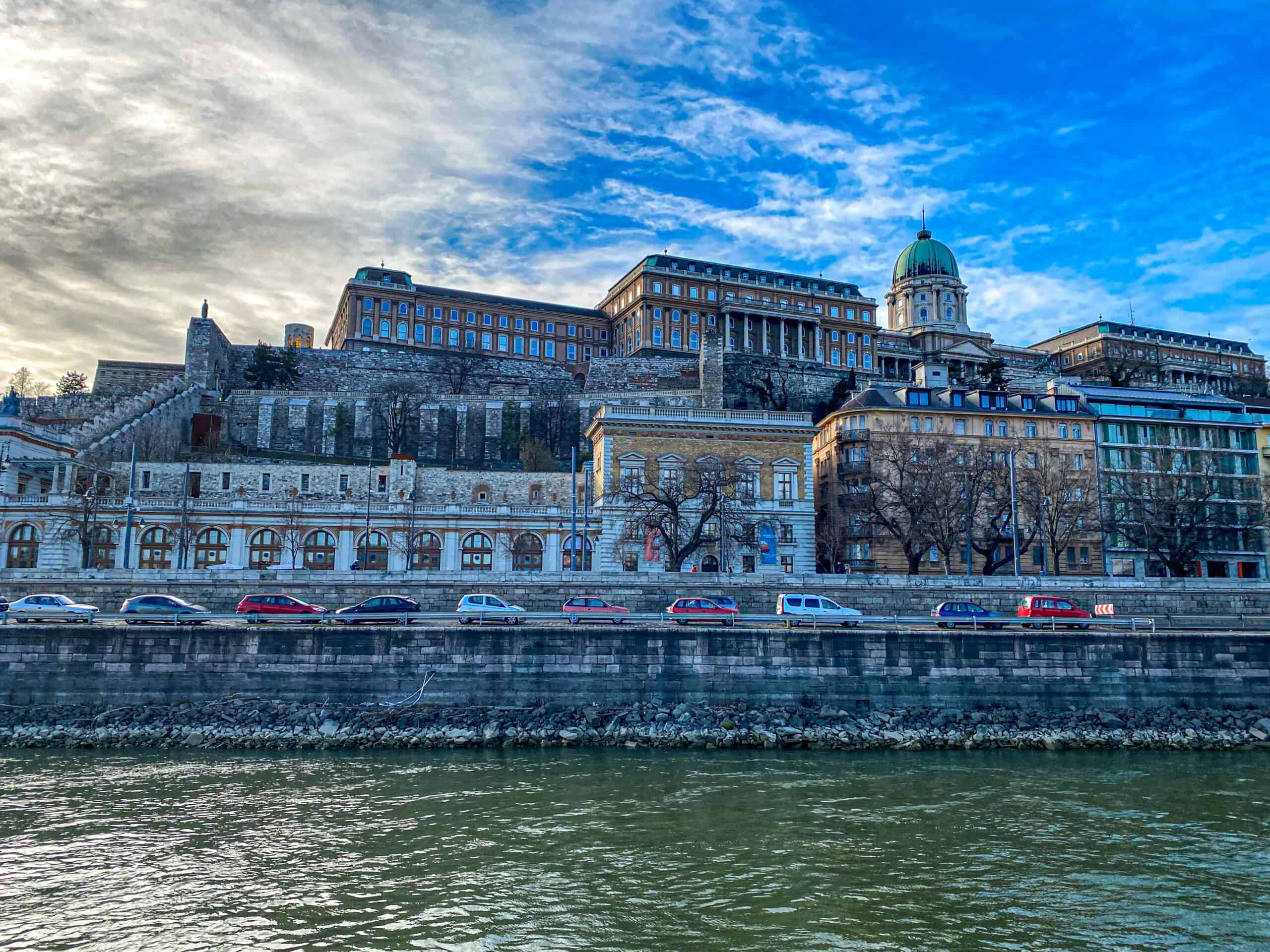 A white boat smoothly navigating the Danube river directly beneath the grand Royal Palace