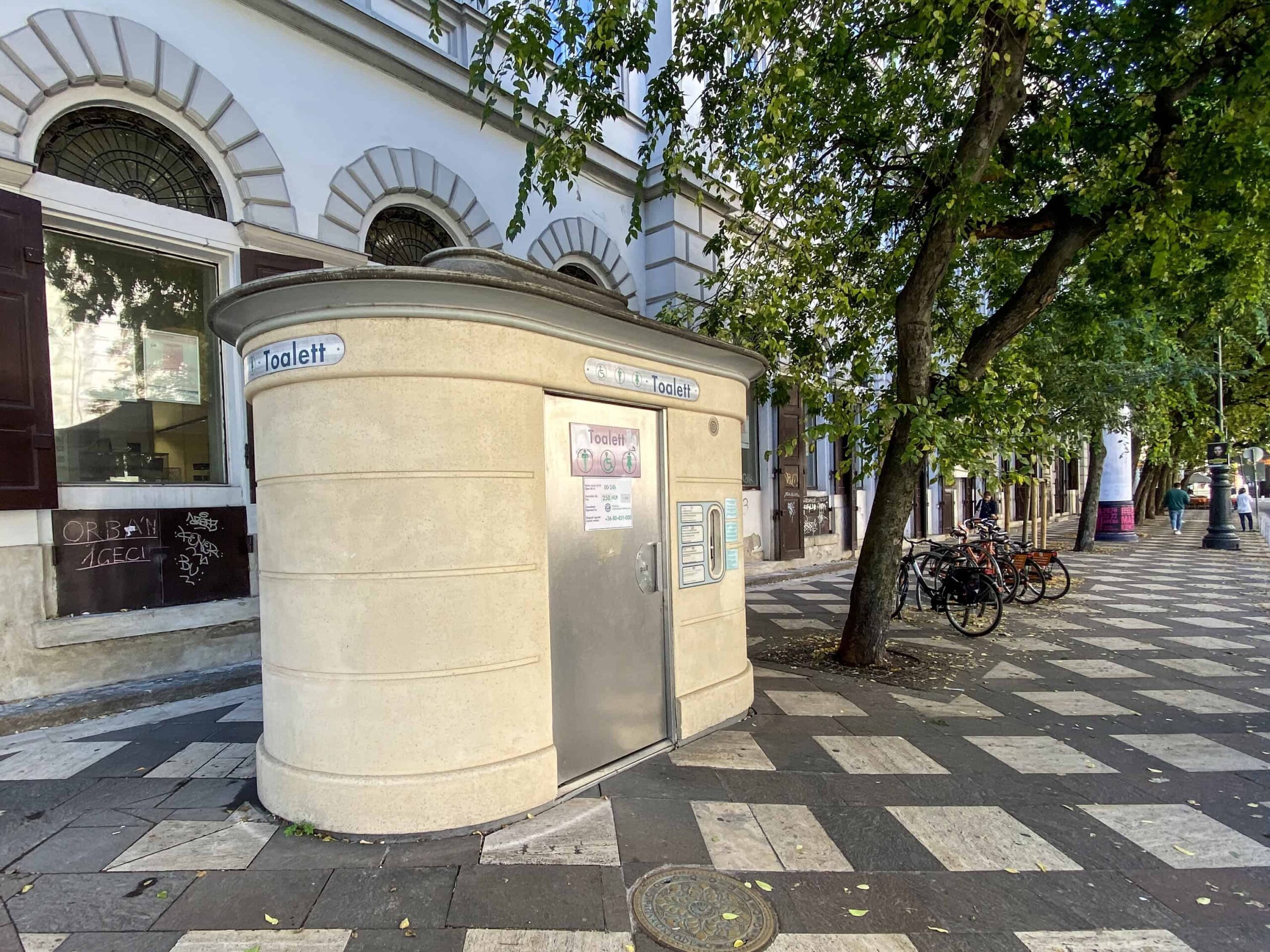 An automated public street toilet booth on a busy sidewalk in Budapest
