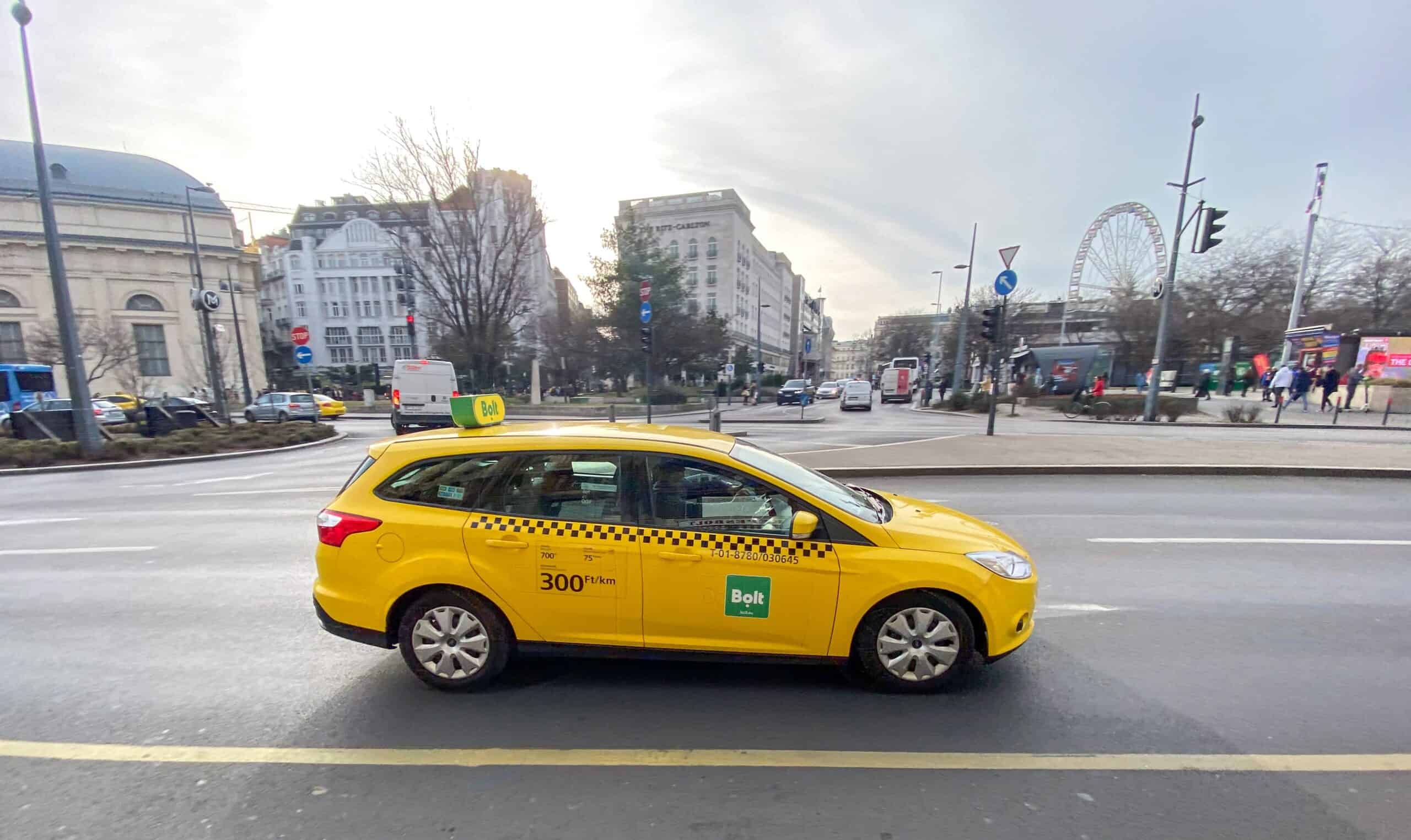 A yellow Bolt taxi driving in the center of Budapest