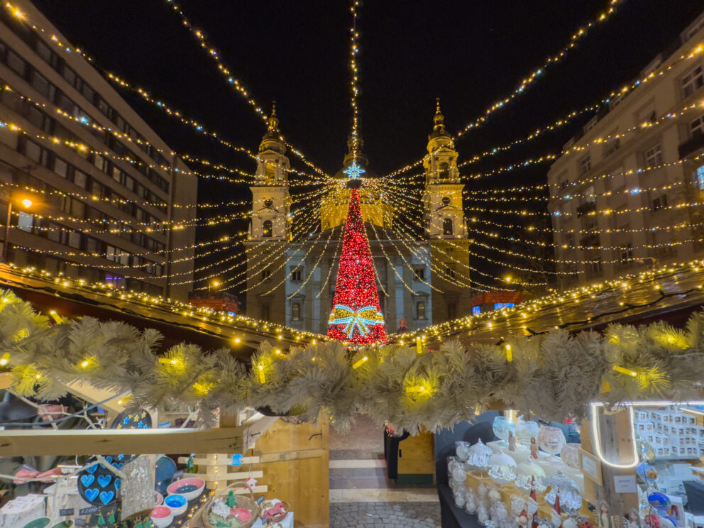The illuminated St. Stephen's Basilica and a bright red Christmas tree at the Advent fair in Budapest.