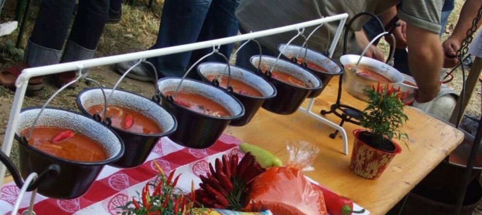 Bowls of traditional spicy Hungarian fish soup on a red checkered tablecloth