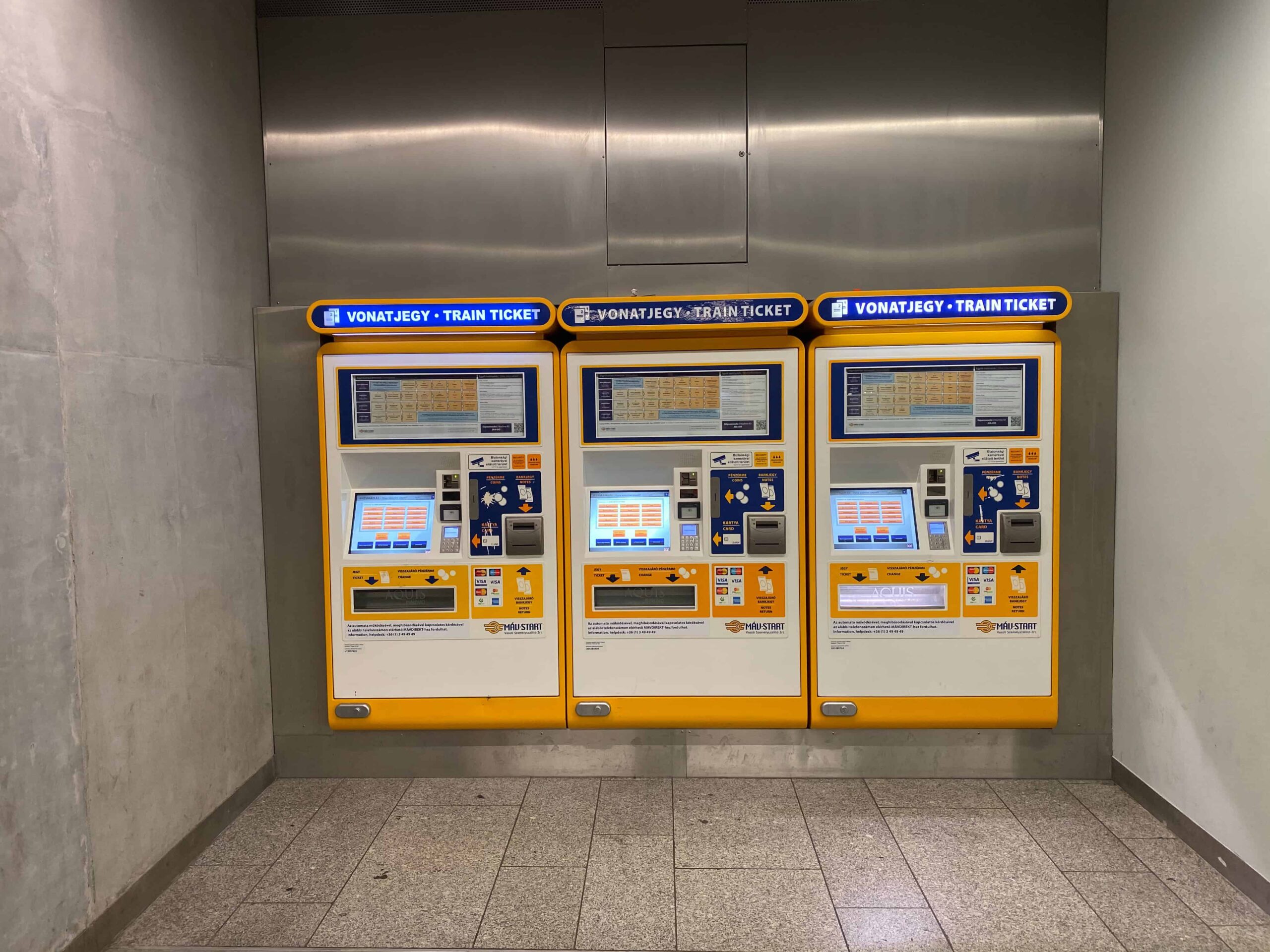 Yellow and blue automated train ticket machines inside a Budapest railway station