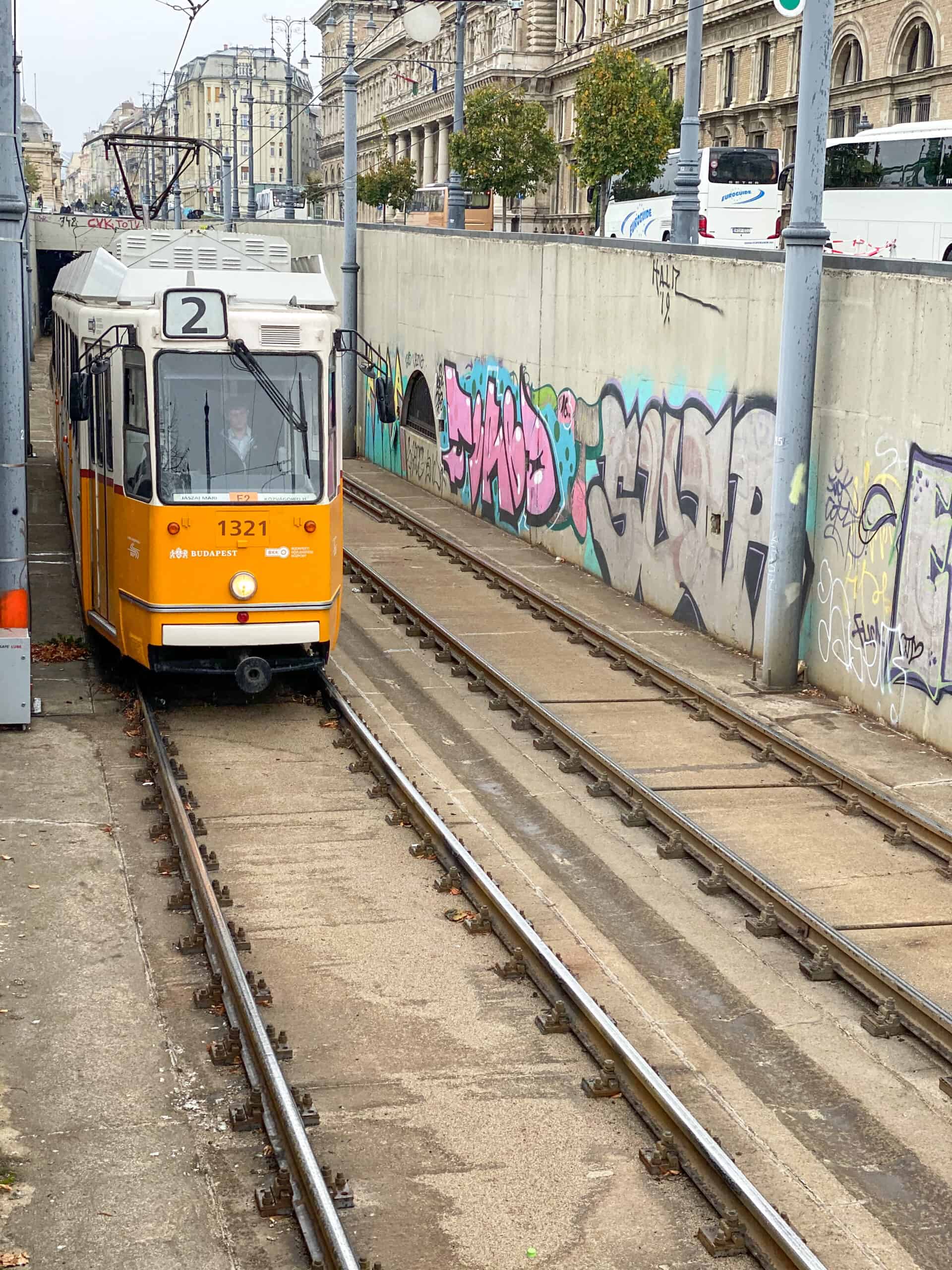 A yellow tram emerging from a graffiti covered underpass in Budapest