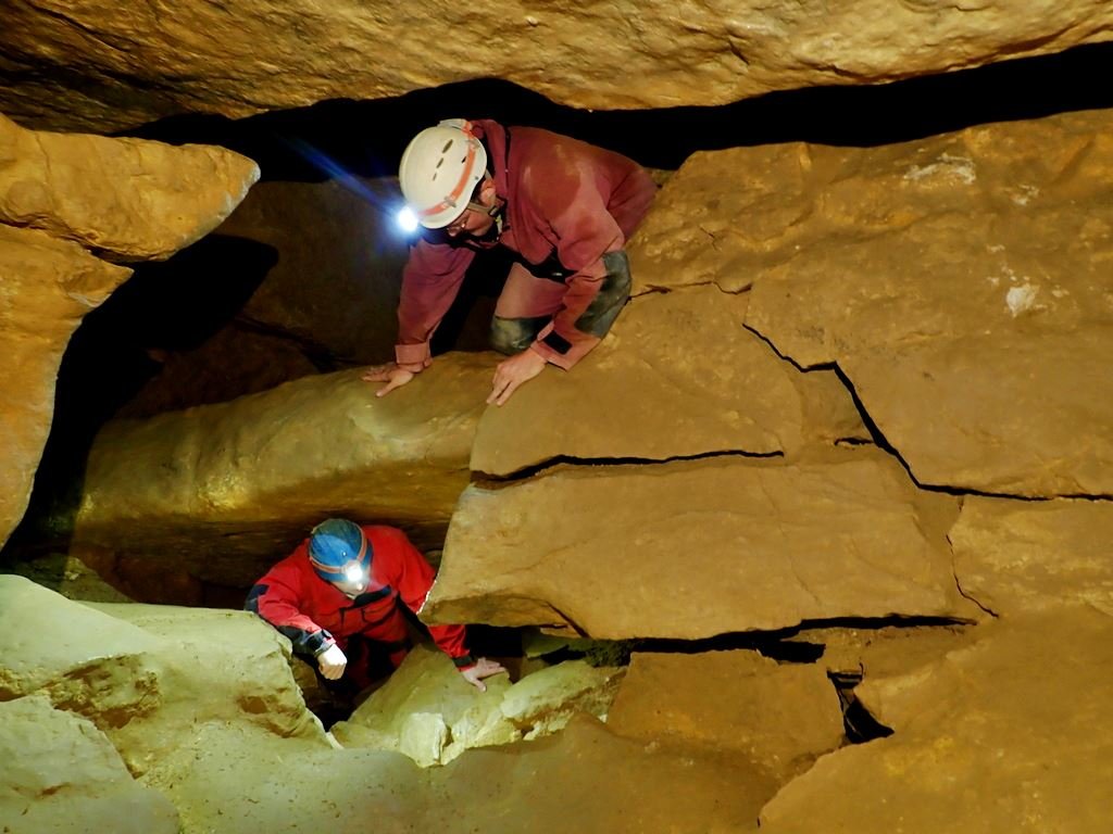 Cavers crawling through holes in the Mátyáshegy cave network