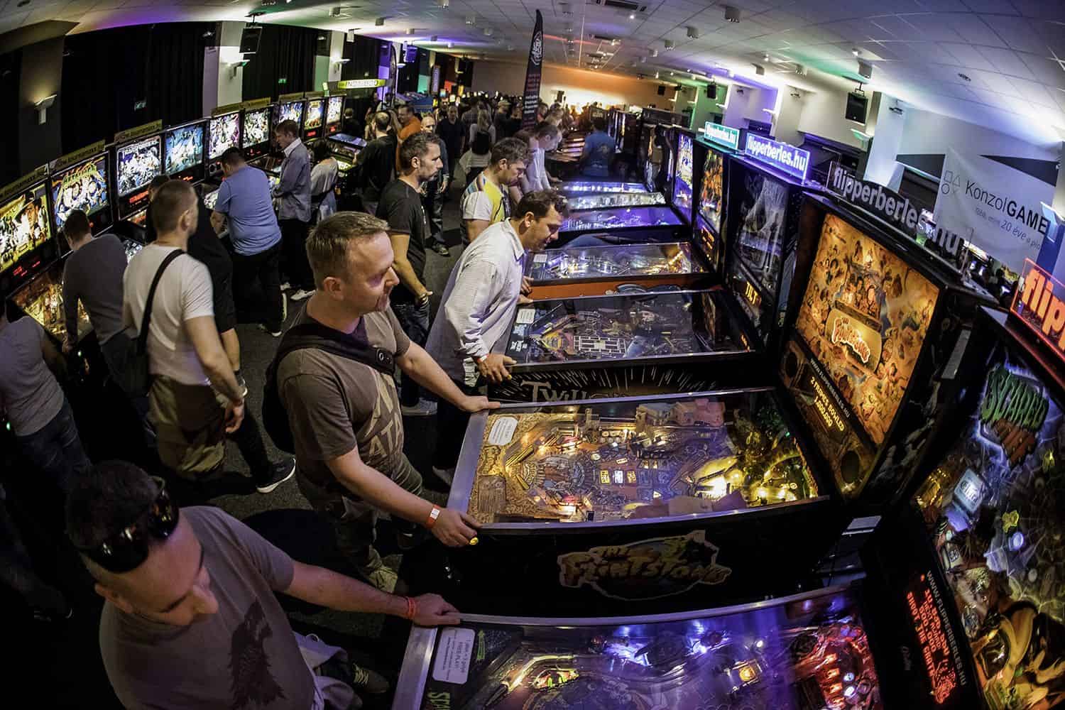 A crowded arcade hall filled with visitors playing along endless rows of pinball machines