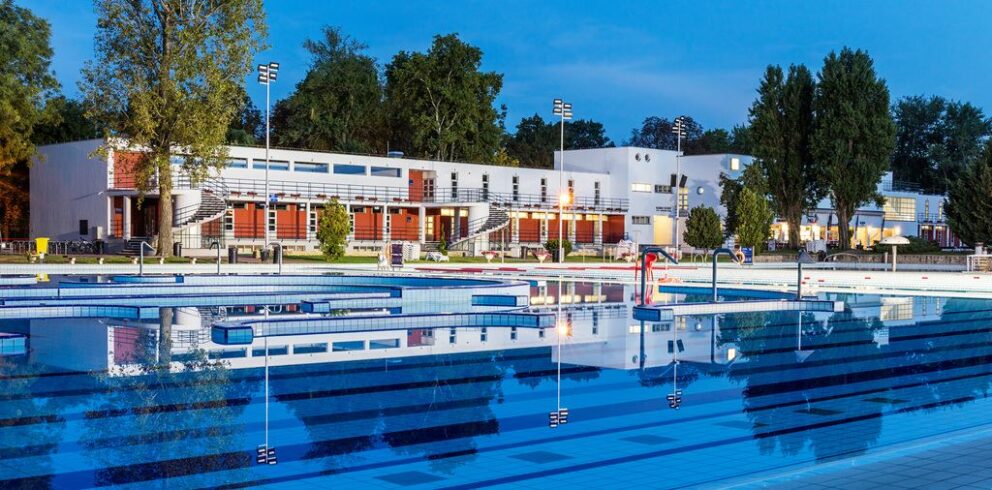 An outdoor swimming pool reflecting a modern white building at twilight
