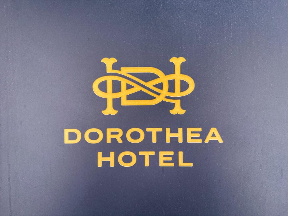 The elegant brass Dorothea Hotel and Autograph Collection logo on the stone wall