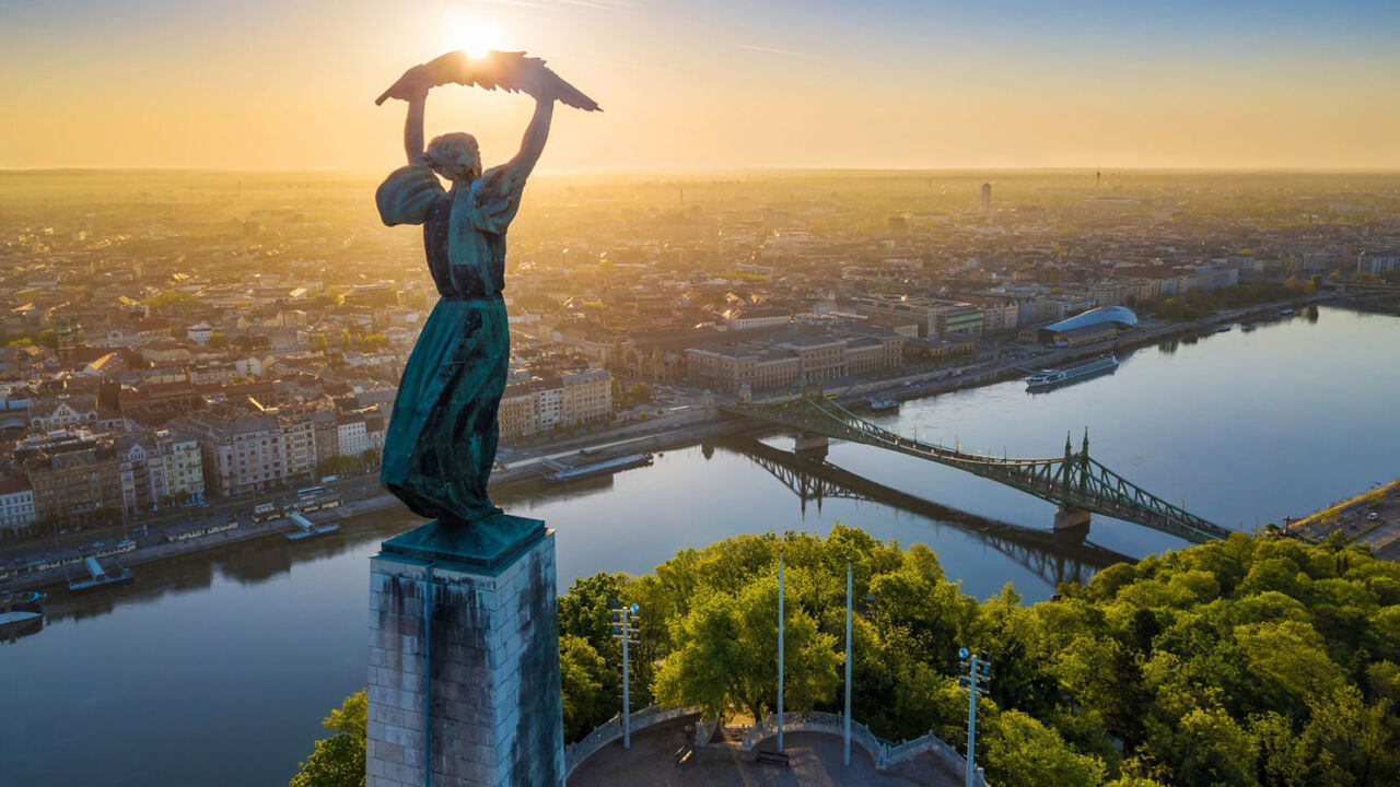 A golden sunrise drone view of the Liberty Statue overlooking the Danube River
