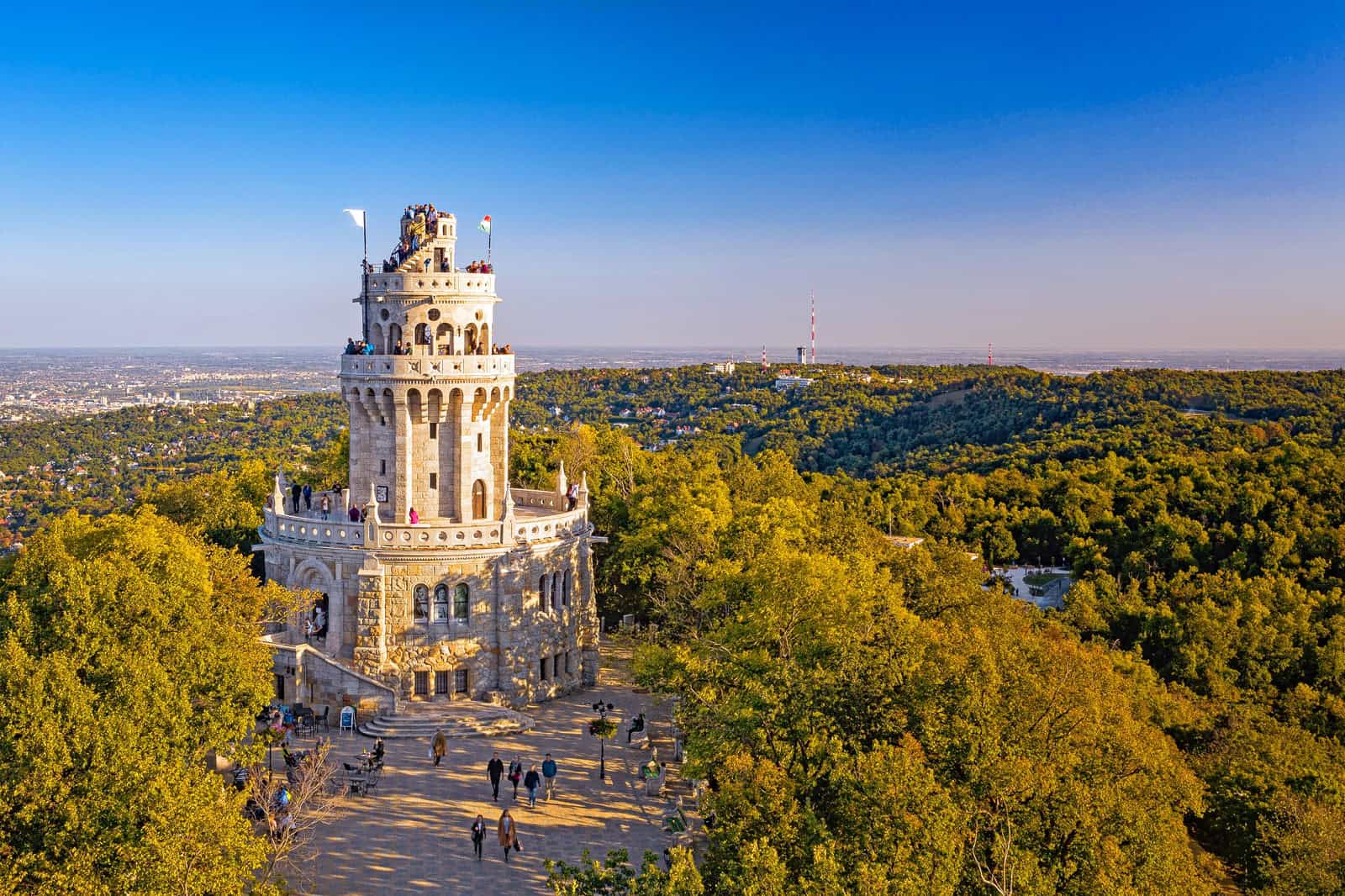 Wide aerial view of the historic Elisabeth Lookout Tower on János-hegy surrounded by lush forests in Budapest.