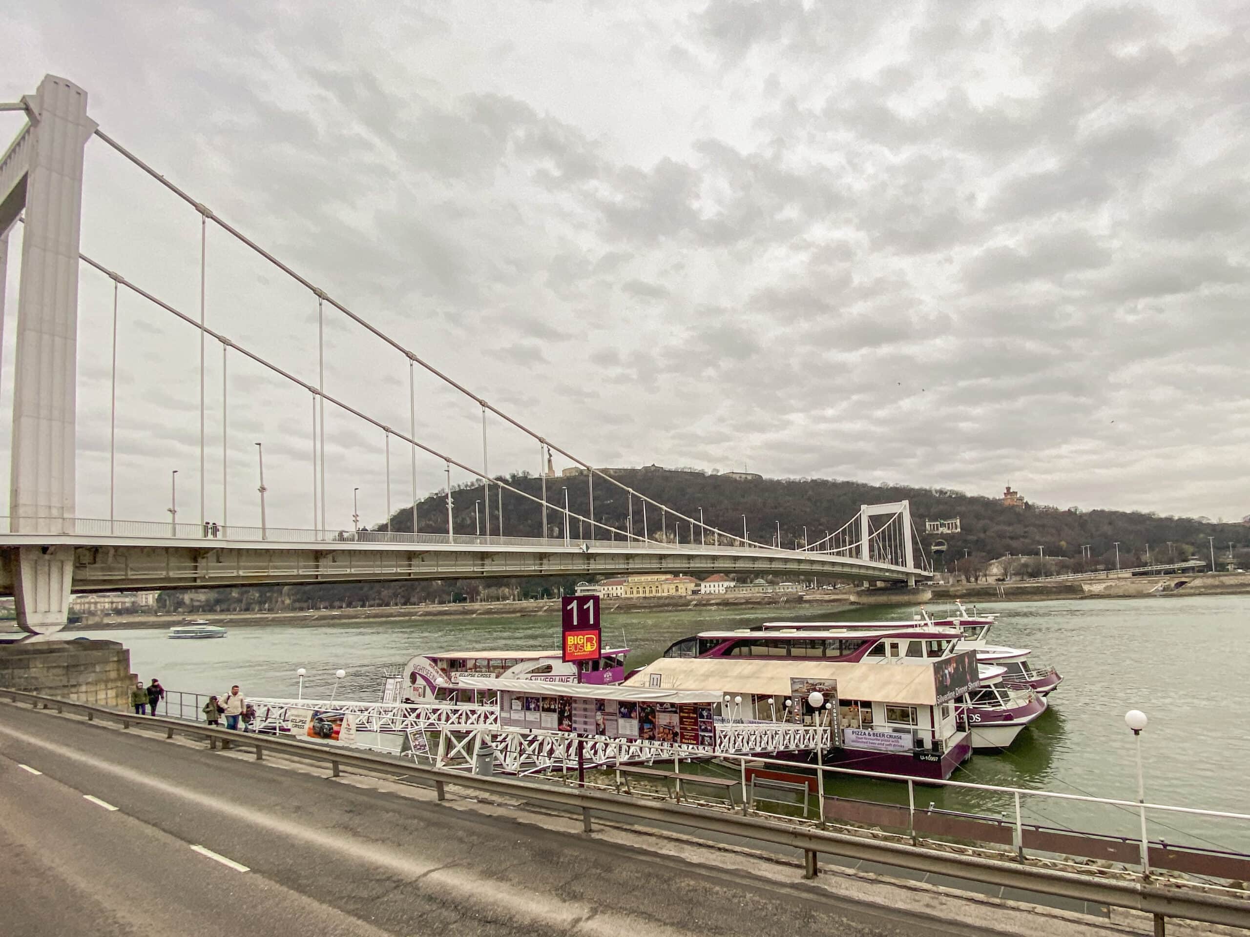 The sleek white Elizabeth Bridge in Budapest and a boat dock on the Danube river bank