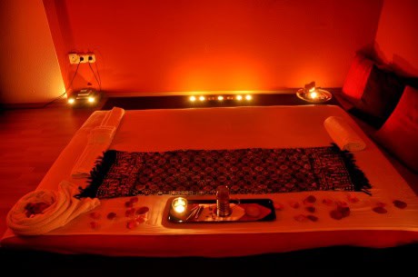 An explicitly carefully prepared soft erotic massage bed heavily lined with candles in a red lit room