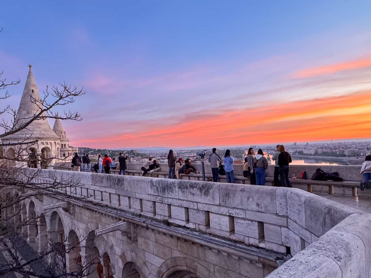 Silhouettes of tourists gathering at the Fisherman's Bastion under a colorful sunset sky