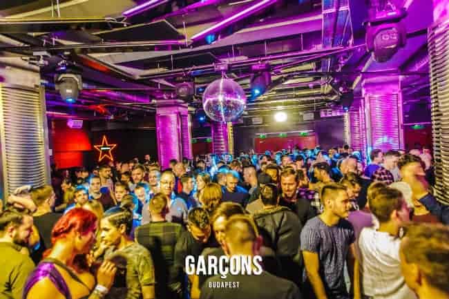 A massive, energetic crowd dancing under intense stage lights at a Garçons party