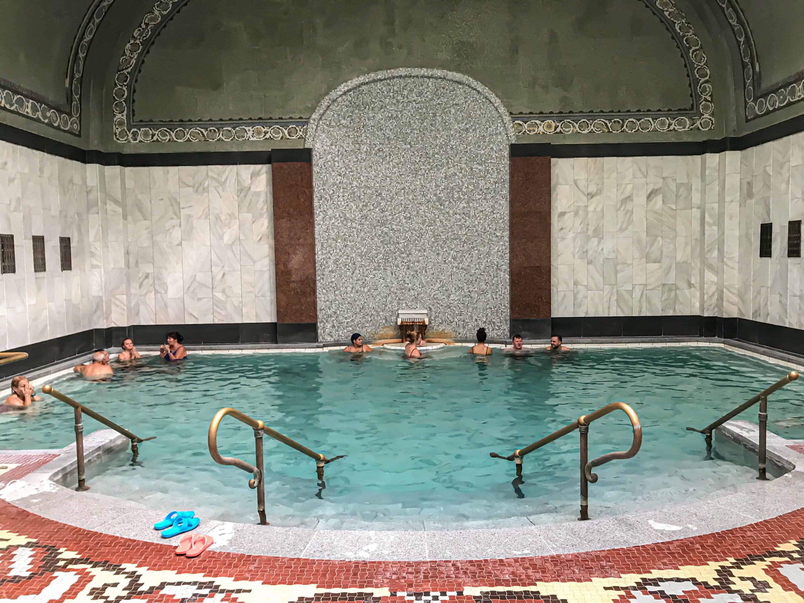 Thermal water pouring from carved stone spouts into an ornate mosaic pool