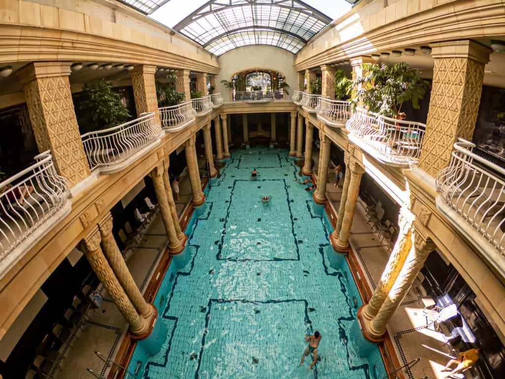 The magnificent Art Nouveau indoor swimming pool of the Gellert Thermal Bath with its iconic stone columns and turquoise water.