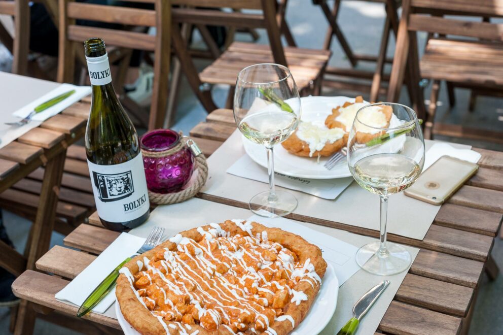 A heavily loaded gourmet Langos served with a bottle of white wine