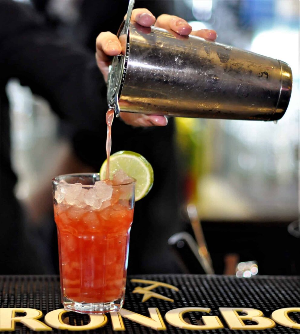 A bartender pouring a brightly colored summer cocktail over ice at the Grund bar
