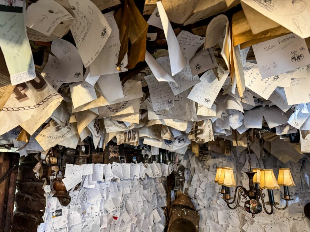 A guest stapling their handwritten paper note to the heavily decorated wall of the pub