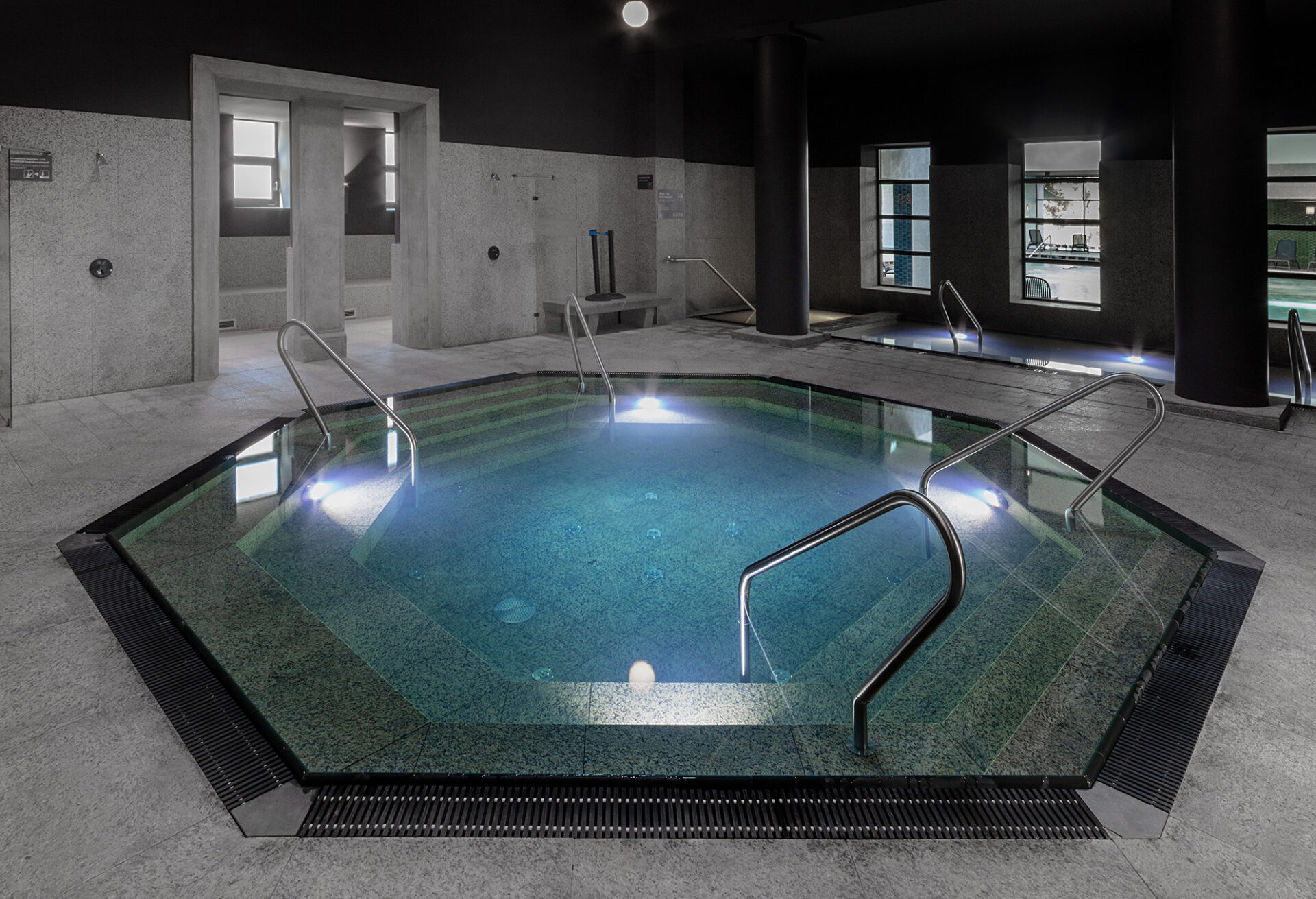A modern hexagonal indoor thermal pool illuminated by blue underwater lights