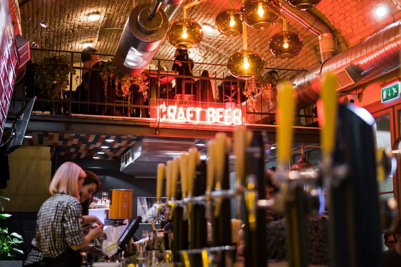 A lively, crowded scene inside Hops Beer Bar with patrons enjoying their drinks