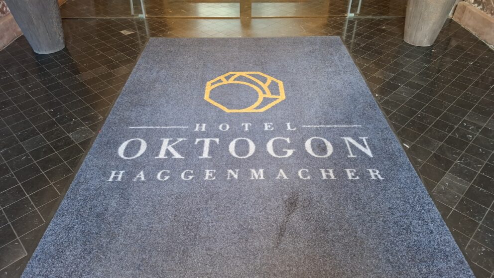 A dark blue entrance floor mat displaying the logo and text Hotel Oktogon Haggenmacher