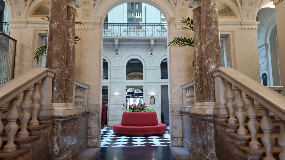 A grand Neo-Renaissance staircase featuring heavy marble columns and a bright red circular velvet seat