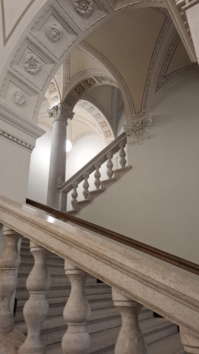 Detailed architecture showing heavy stone balusters and painted arches at the Hotel Oktogon