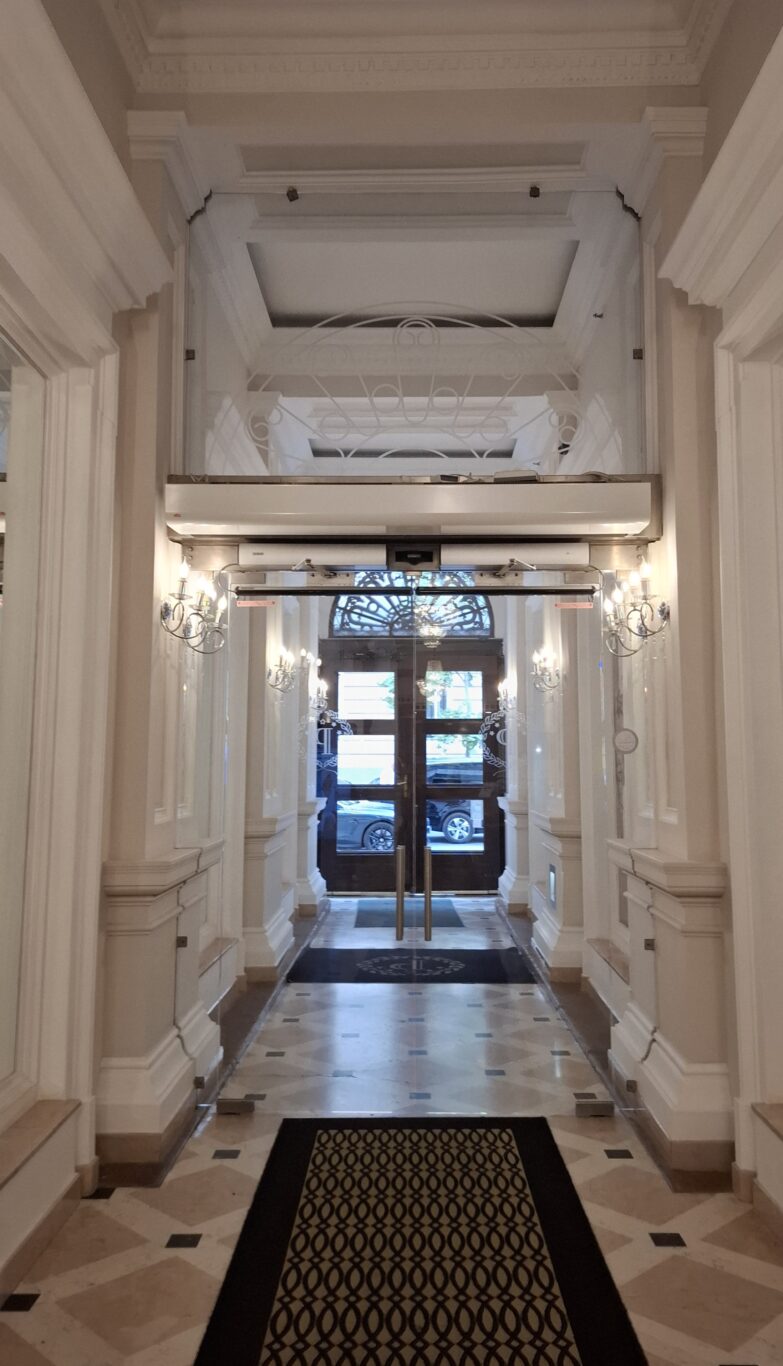 The elegant, brightly lit corridor leading to the glass entrance doors of the hotel
