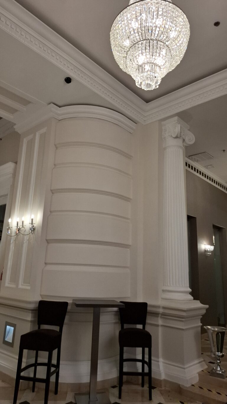 A glowing globe-shaped crystal chandelier hanging from an ornately molded ceiling