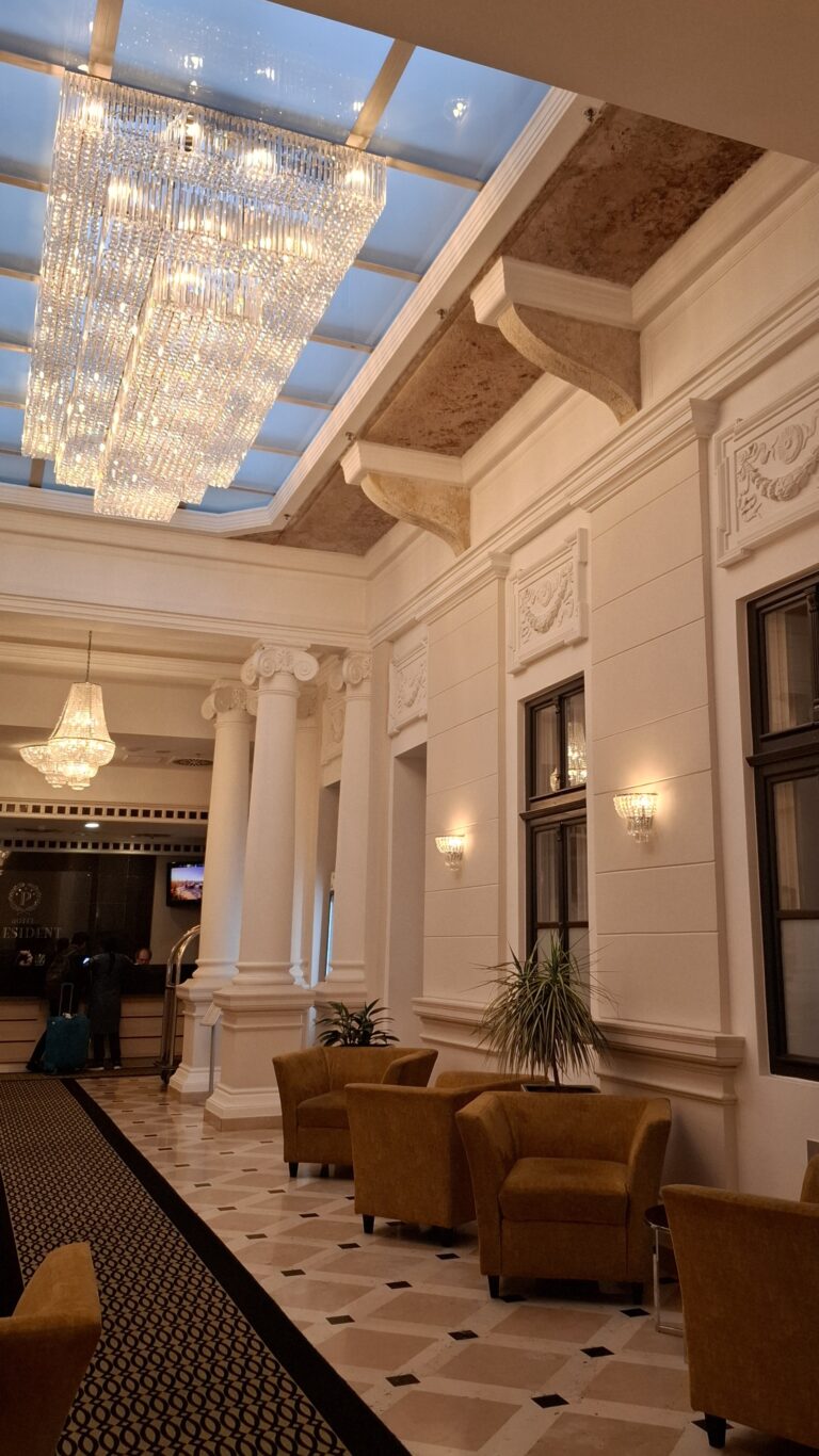 A massive rectangular crystal chandelier hanging beneath a glass skylight in the hotel lobby