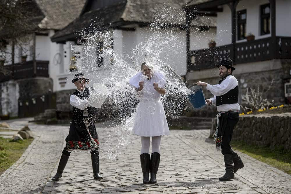 Two men in traditional costumes throwing buckets of water on a woman for Easter Monday