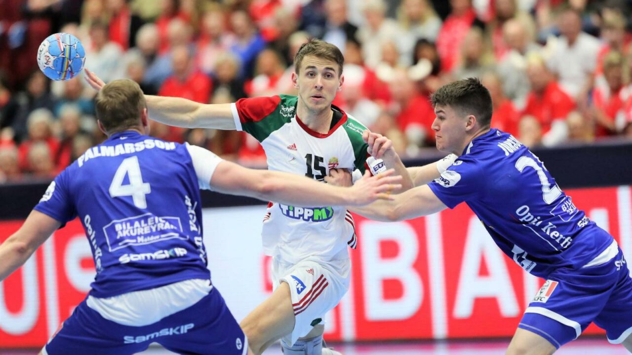 A Hungarian handball player jumping to shoot while defended by two Icelandic players
