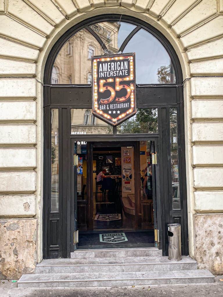 The glass main entrance and dark awnings of I55 American Bar from the street