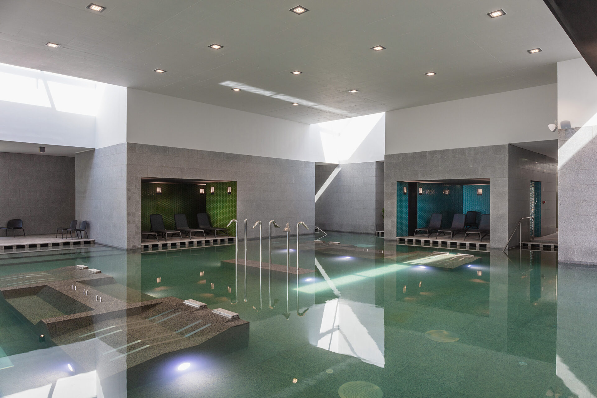 A modern indoor thermal pool featuring submerged stone lounge beds