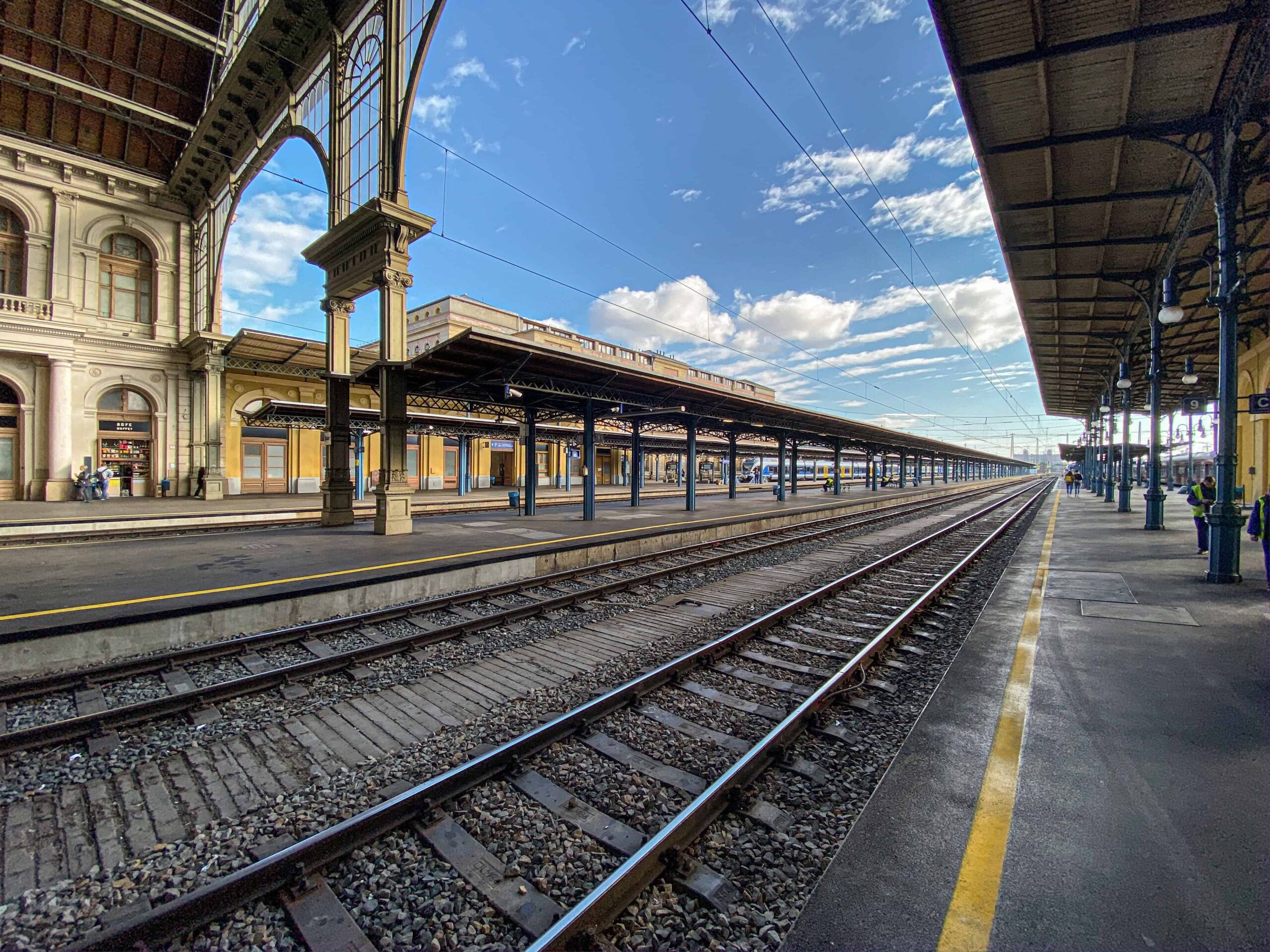 Travelers rolling luggage alongside an international train inside Keleti Station