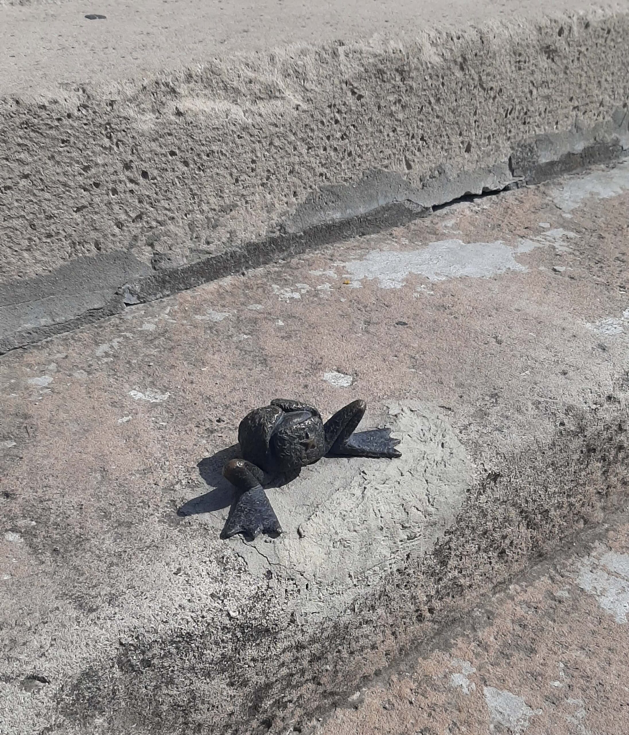 A charming detailed miniature bronze sculpture securely attached to a stone railing overlooking the Danube river