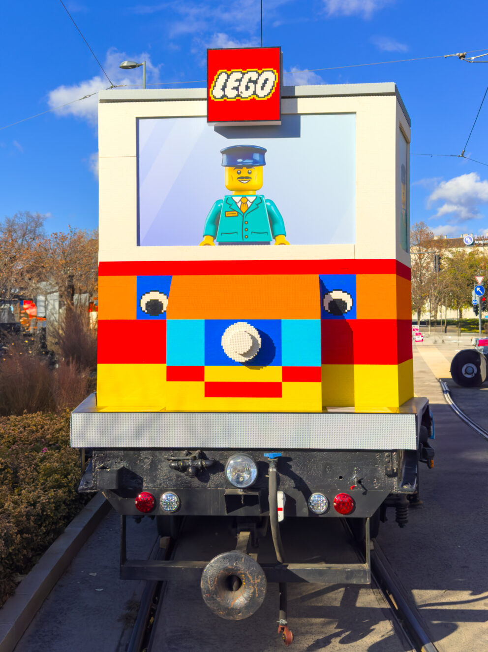 A male LEGO character figure with a uniform securely operating the massive tram