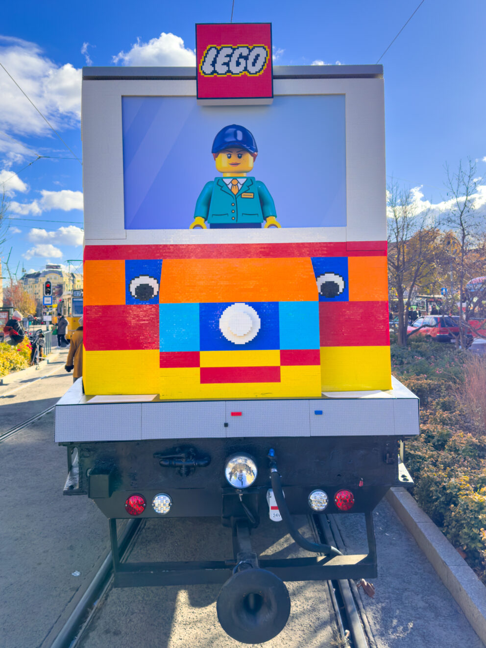 A female LEGO character constructed of colored bricks actively driving the tram
