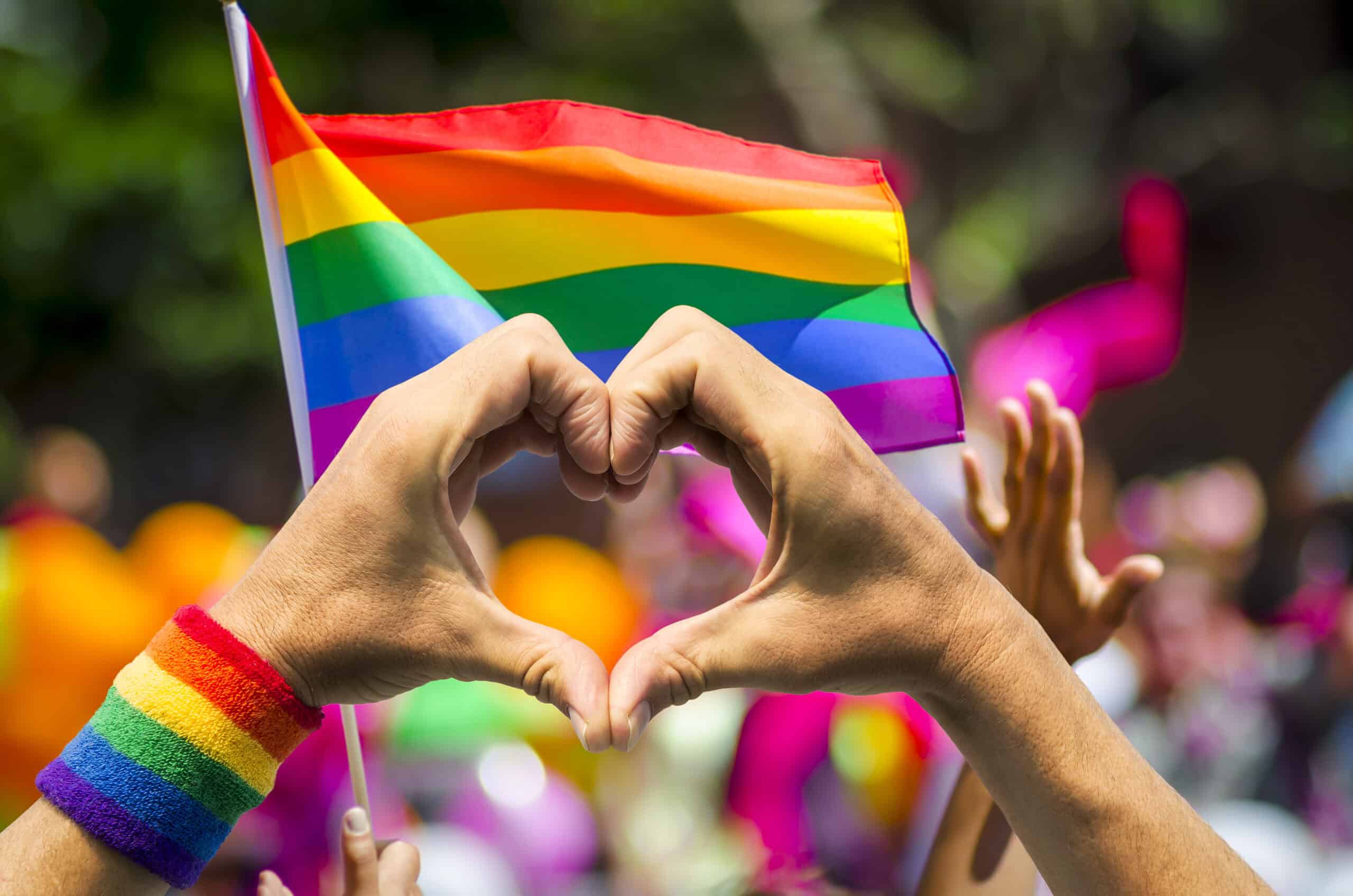 A vibrant rainbow Pride flag waving against a clear blue sky