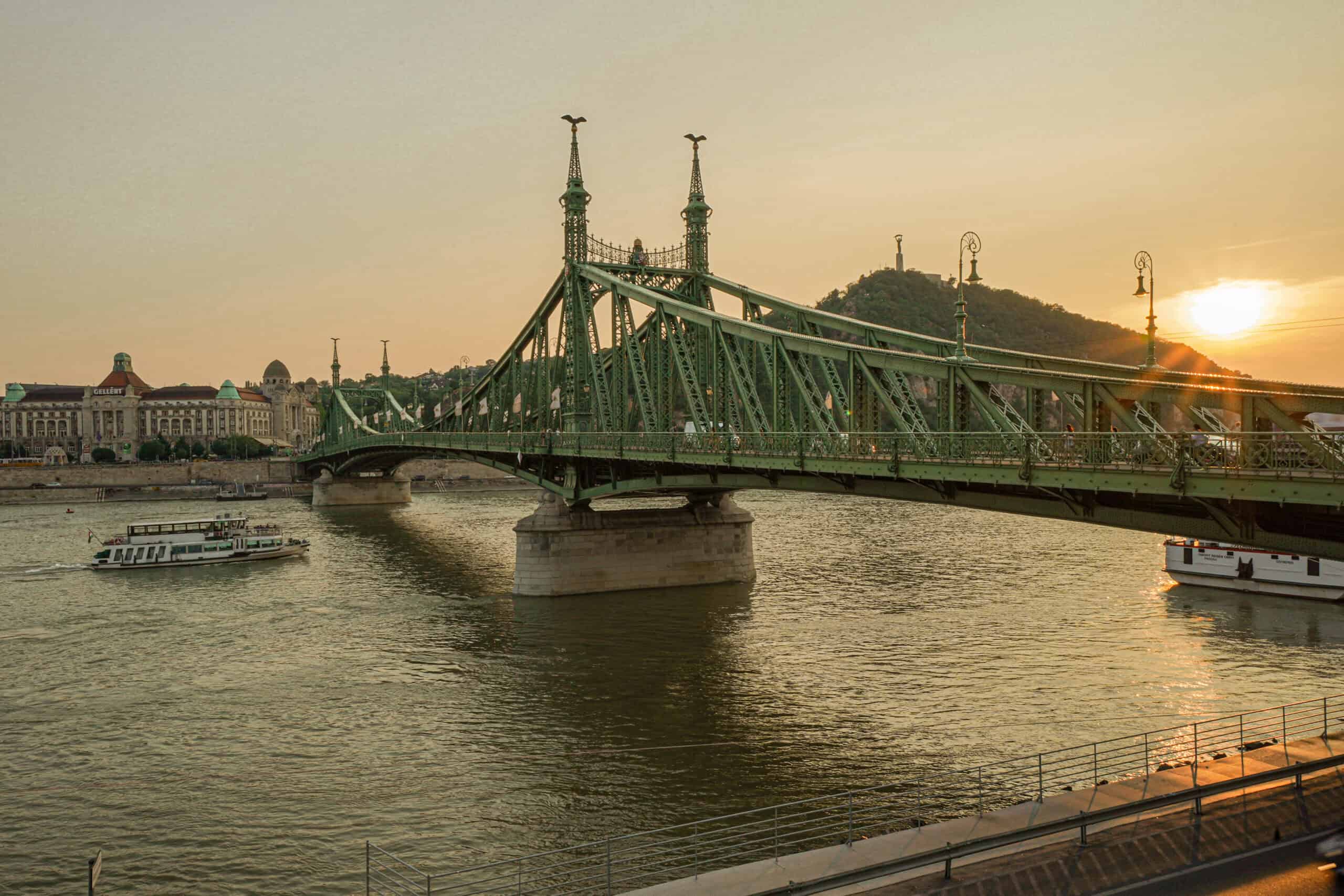 The green wrought iron structure of Liberty Bridge glowing softly warmly during a beautiful sunset