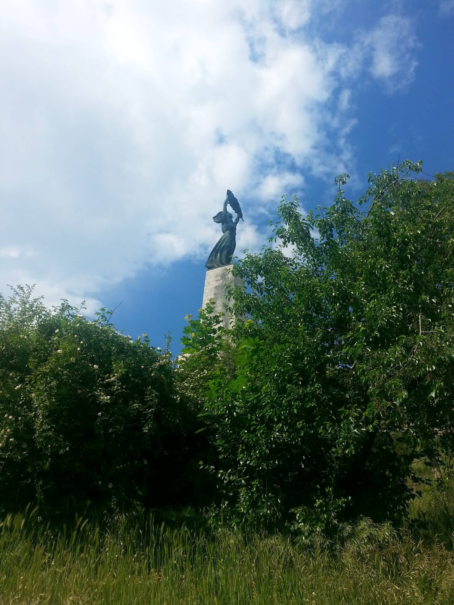 The iconic Liberty Statue on top of Gellert Hill seen from below towering over green trees