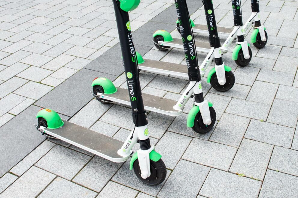 Several Lime electric scooters parked next to each other on a paved sidewalk