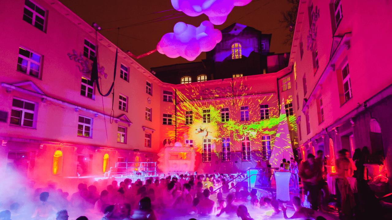 Vibrant neon lights reflecting on the steam over the crowd at the Lukács Bath party